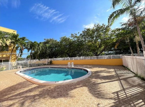 Outdoor swimming pool with tiled surround and metal fence.