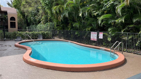 Outdoor swimming pool surrounded by foliage and a fence.