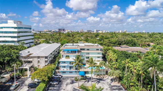 Elevated view of apartment complexes with surrounding greenery and cityscape in the background.