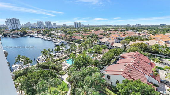 Panoramic view of a marina and residential area with boats, trees, and houses with red roofs.