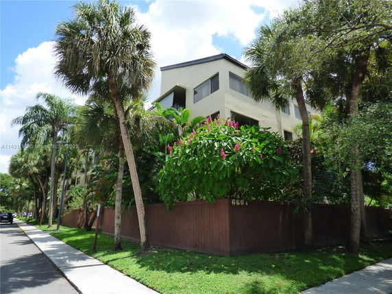 Front view of a multi-story building with surrounding palm trees and a wooden fence.