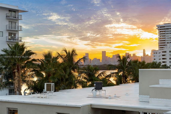 Rooftop with air conditioning units and a view of a city skyline at sunset.
