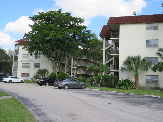 Front view of a mid-rise apartment building with outdoor staircases and parking area in front.