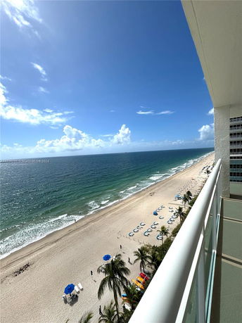 View from a high-rise building's balcony overlooking a beach and the ocean.