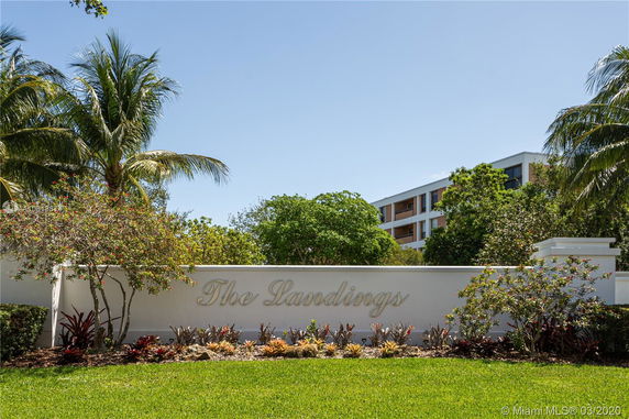 View of a building partially hidden by trees with a white sign reading 'The Landings' in the foreground.