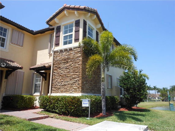 Front view of a two-story townhouse with stone accents and a palm tree in front.