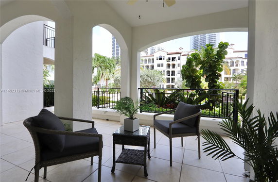 View from a balcony with chairs and plants, overlooking an apartment complex with arches and greenery.