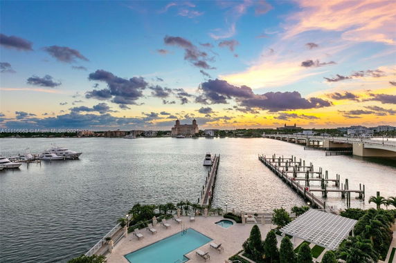 Panoramic view of a waterfront area with a pool and docks, overlooking a body of water and a distant skyline at sunset.