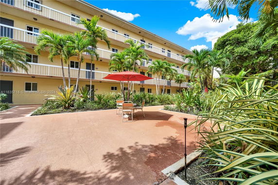 Outdoor view of a multi-story building with balconies and a patio area with umbrella and chairs.