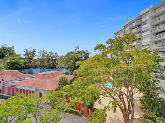 View of a multi-story building with balconies and a nearby lake surrounded by trees.