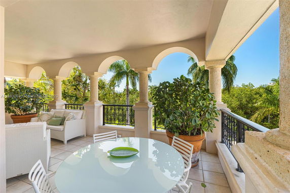 Covered outdoor patio with arches and seating, overlooking palm trees.