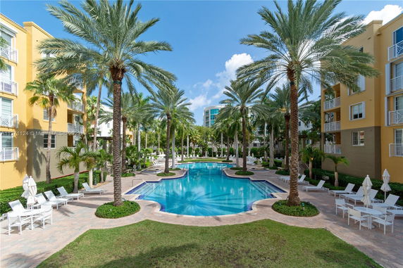 Outdoor swimming pool surrounded by palm trees and apartment buildings.