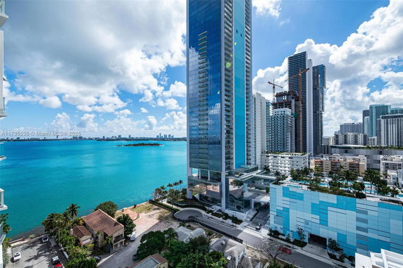 Scenic view of high-rise buildings by a large body of water under a partly cloudy sky.