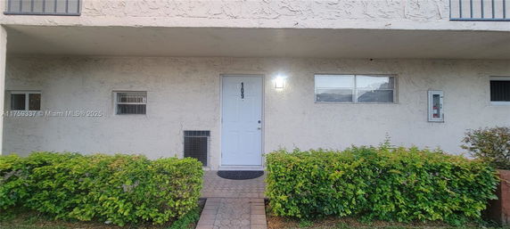 Front view of a residential building entrance with a white door and adjacent windows.