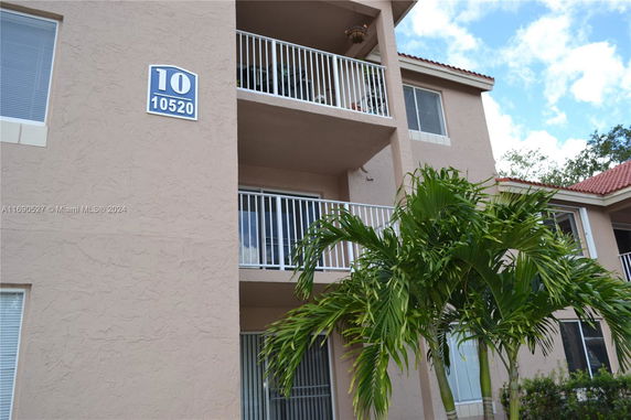 Front view of a multi-story building with balconies and a palm tree.