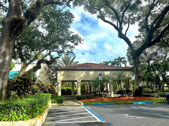 Front view of a building with a tiled roof and columns, surrounded by trees and landscaping.
