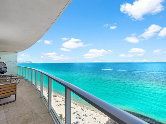 Panoramic beach view from a high-rise balcony with glass railing.