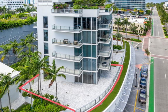Front view of a modern multi-story building with glass balconies and a rooftop garden.