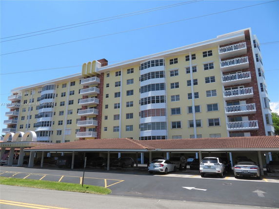 Front view of a multi-story residential building with balconies and a covered parking area below.