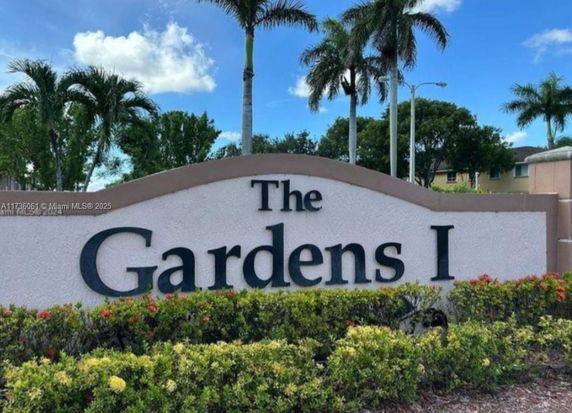 Sign displaying 'The Gardens I' with palm trees and sky in the background.