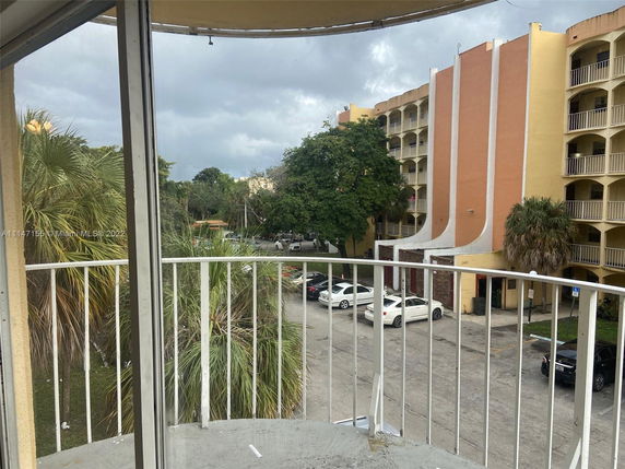 View from a balcony showing a multi-story apartment building with orange facade and balconies, surrounded by trees and parked cars.