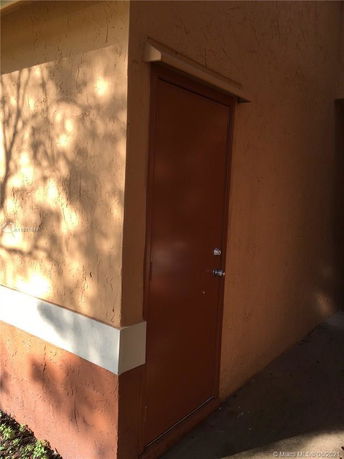 View of a portion of a building with a brown door and textured walls.
