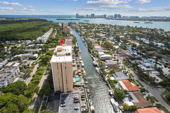 Aerial view of a canal-side residential area with a tall building and surrounding homes, with a view of water and greenery.