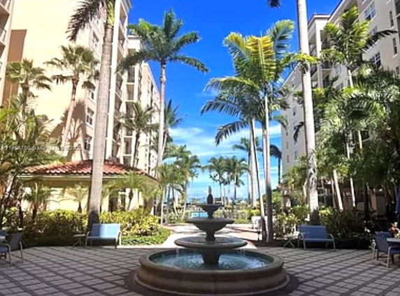 View of two adjacent multi-story buildings with palm trees and a fountain in the foreground.
