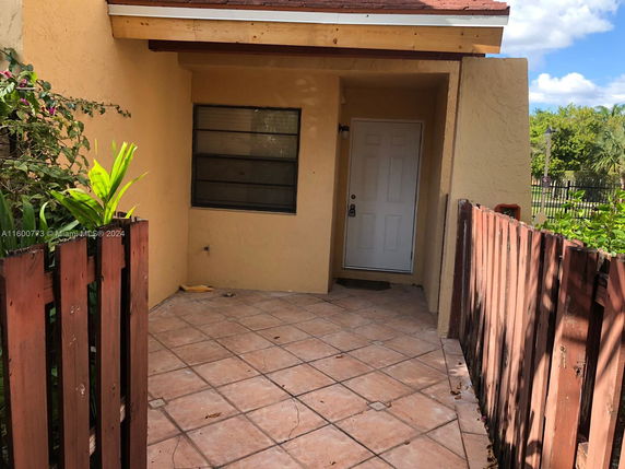 Front view of a house entrance with a tiled patio and wooden fence.
