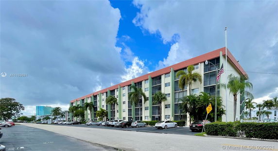 Front view of a multi-story residential building with a red roof and palm trees.
