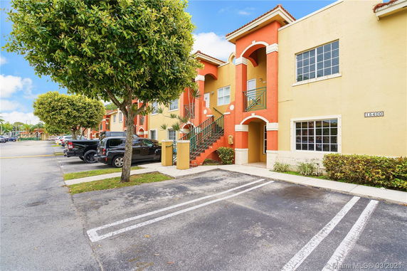 View of an apartment building with parking spaces and trees.