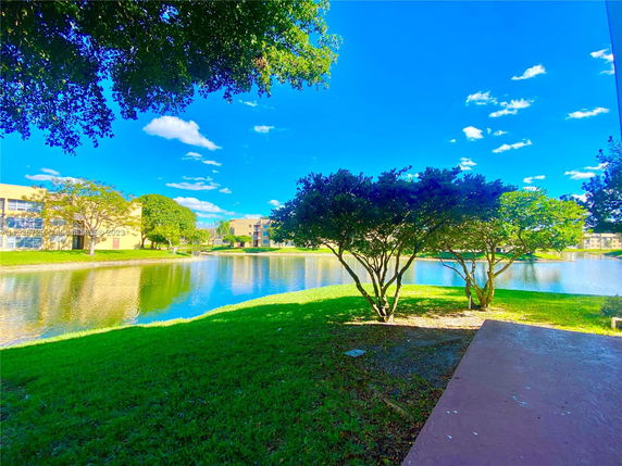 View of apartment buildings surrounding a small lake with trees and greenery.