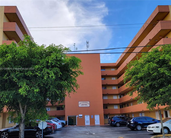 Front view of a multi-story condominium building with parking area in front.