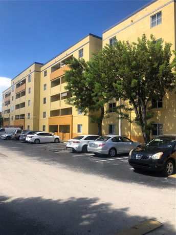 Outdoor parking area in front of a multi-story yellow residential building.