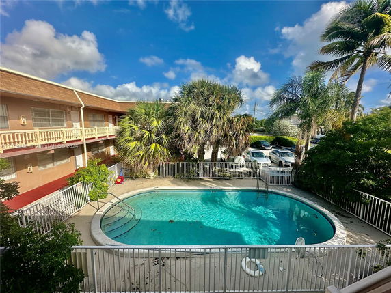 Outdoor swimming pool surrounded by a building and palm trees.
