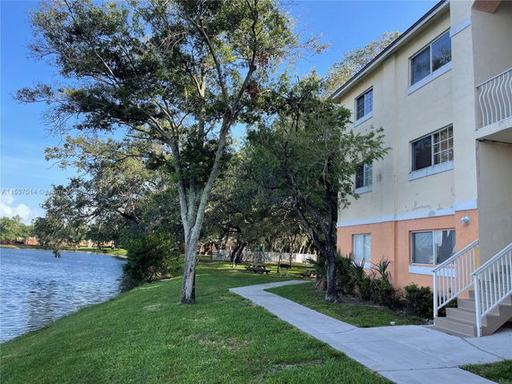 Side view of a multi-story building near a body of water and trees.