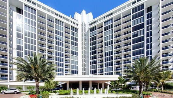 Front view of a multi-story modern apartment building with extensive glass windows and a wide entrance.