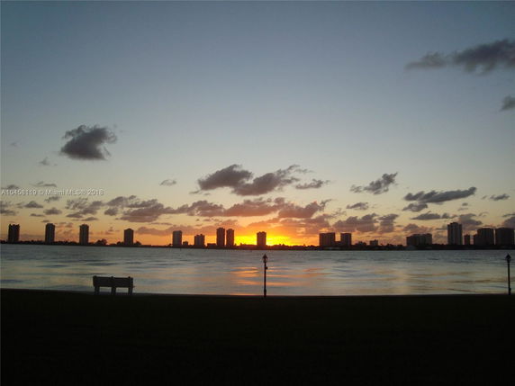 Panoramic view of a sunset over a body of water with several tall buildings silhouetted against the sky.