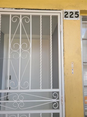 Front view of a building entrance with a white metal security door and yellow exterior wall.
