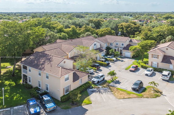 Aerial view of residential buildings surrounded by trees and parking spaces.