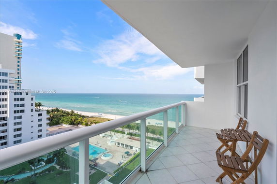 Balcony view overlooking the ocean with nearby buildings and a swimming pool.