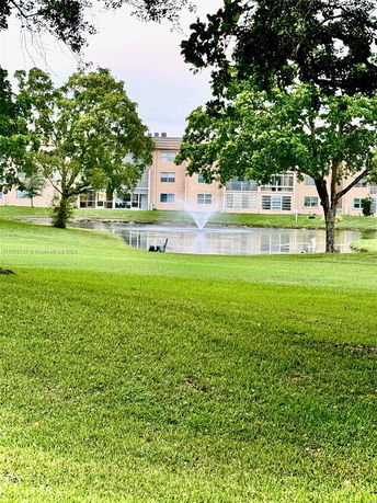 View of a building with large windows and a pond with a fountain in the foreground.