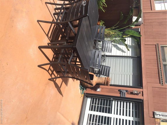 Outdoor area with a large black table and chairs near a sliding glass door entrance to a building.