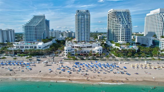 Aerial view of coastal high-rise buildings next to a beach with umbrellas and people.