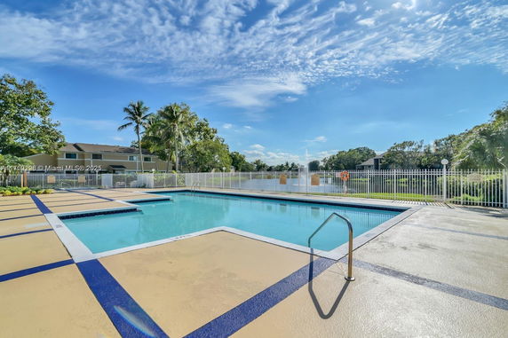 Outdoor swimming pool area with surrounding fence and landscaped trees.