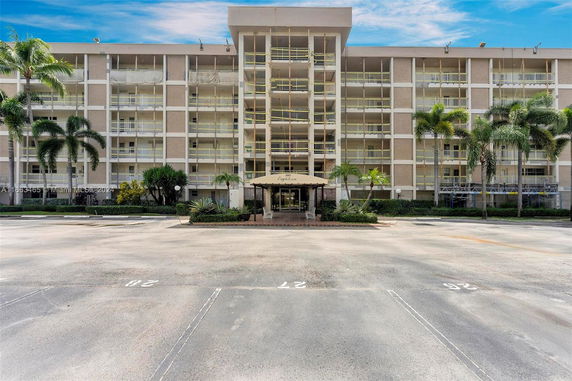 Front view of a mid-rise apartment building with multiple balconies and a central entrance canopy.