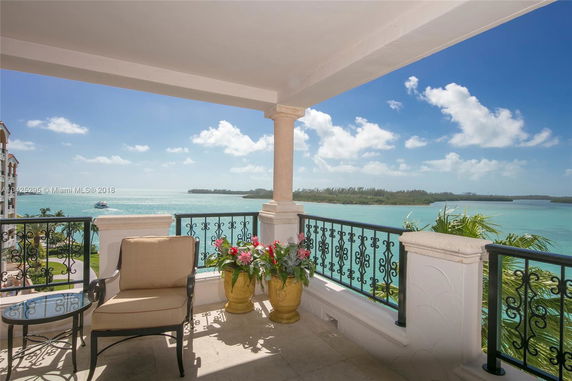 View from a balcony overlooking a body of water with distant land, featuring a chair, table, and decorative balustrade.