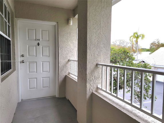 View of a building entrance with a white door and balcony railings overlooking nearby rooftops and trees.