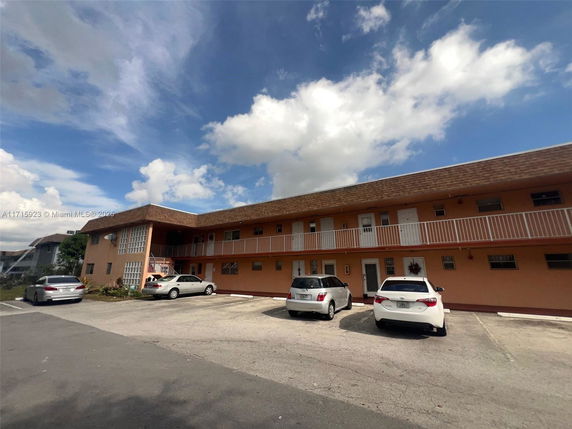 Front view of a two-story apartment building with adjacent parking spaces.