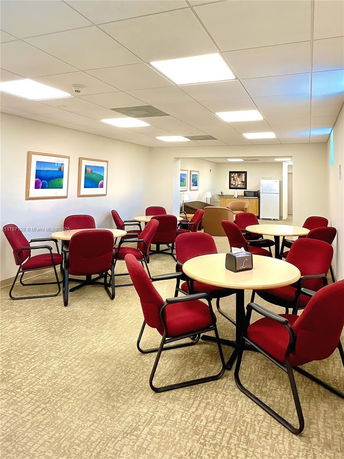 Room with round tables and red chairs, featuring a fridge and a comfortable seating area.
